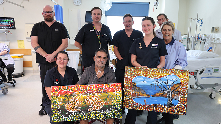 Medical team in ward with patient holding 2 paintings