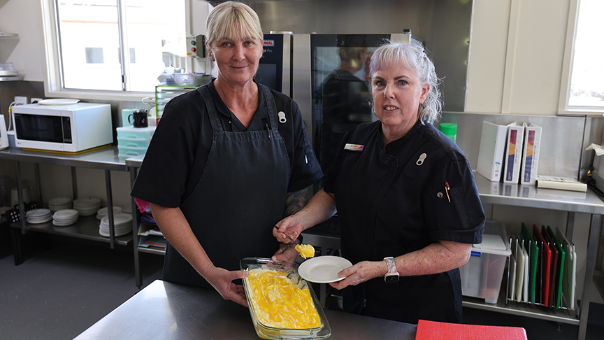 Two cooks in a kitchen holding a dish of food